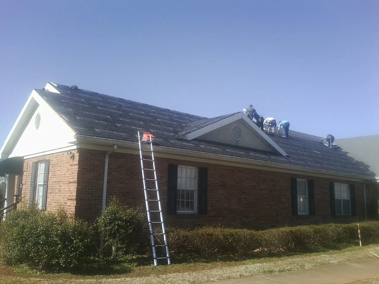 Crew tearing shingles off a brick ranch roof with a ladder set — Emergency Roof Repair work by our crew in Thaxton