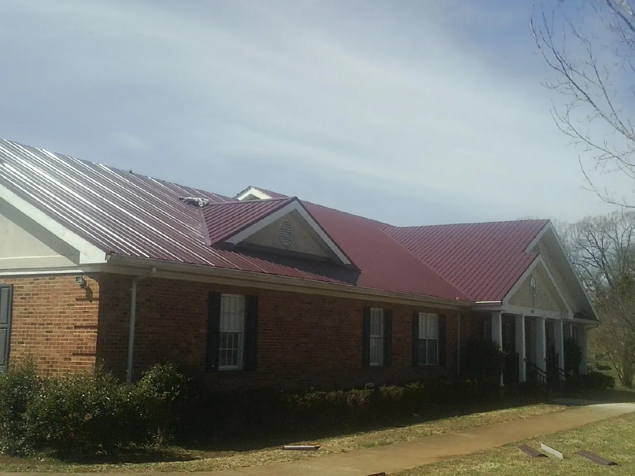 Red metal roof with gabled entries on a long brick building, from a Hail Damage Roof Repair job in Thaxton