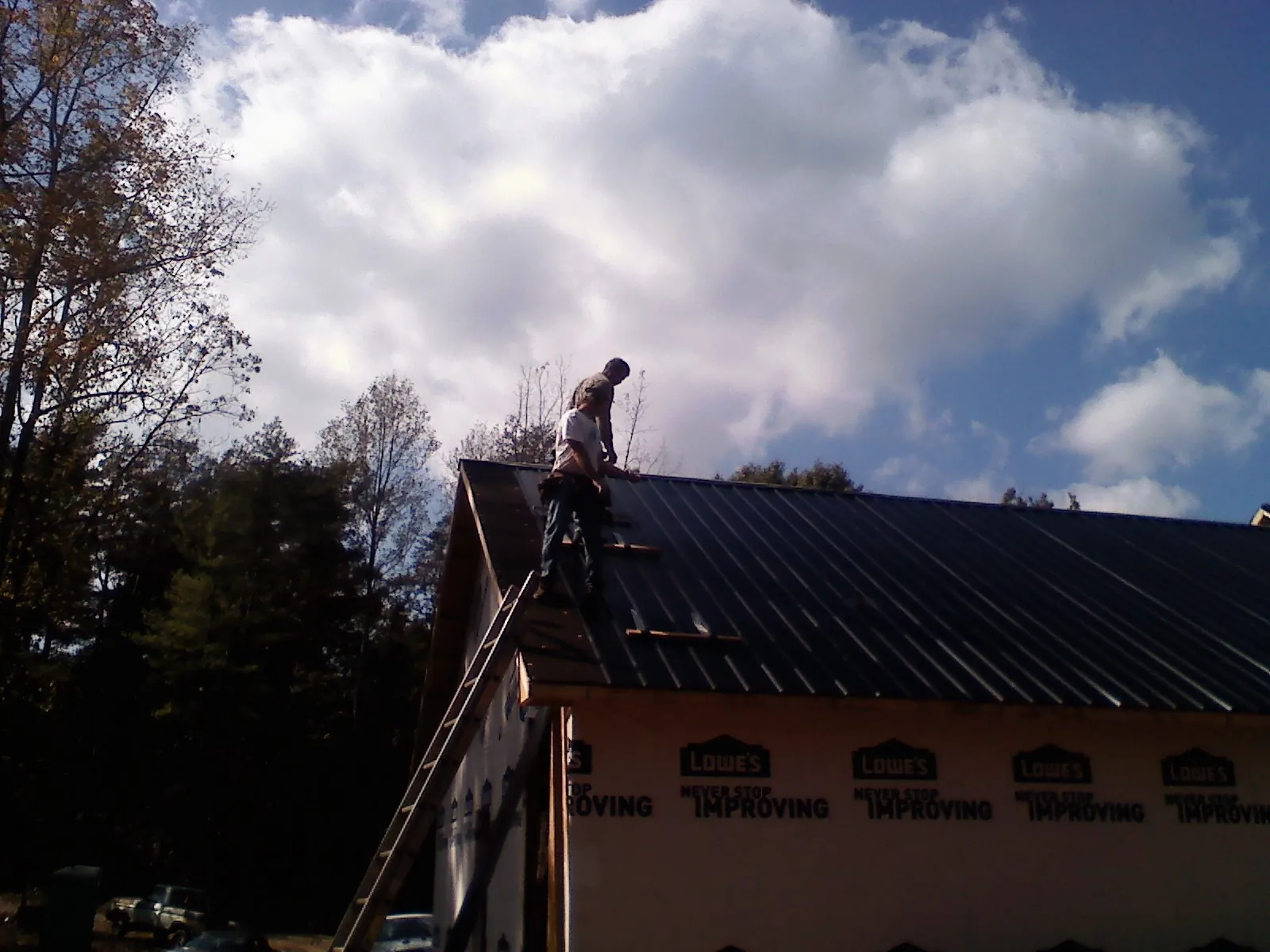 Roofer fastening dark metal panels high against a cloudy sky, from a Roof Inspection job in Thaxton