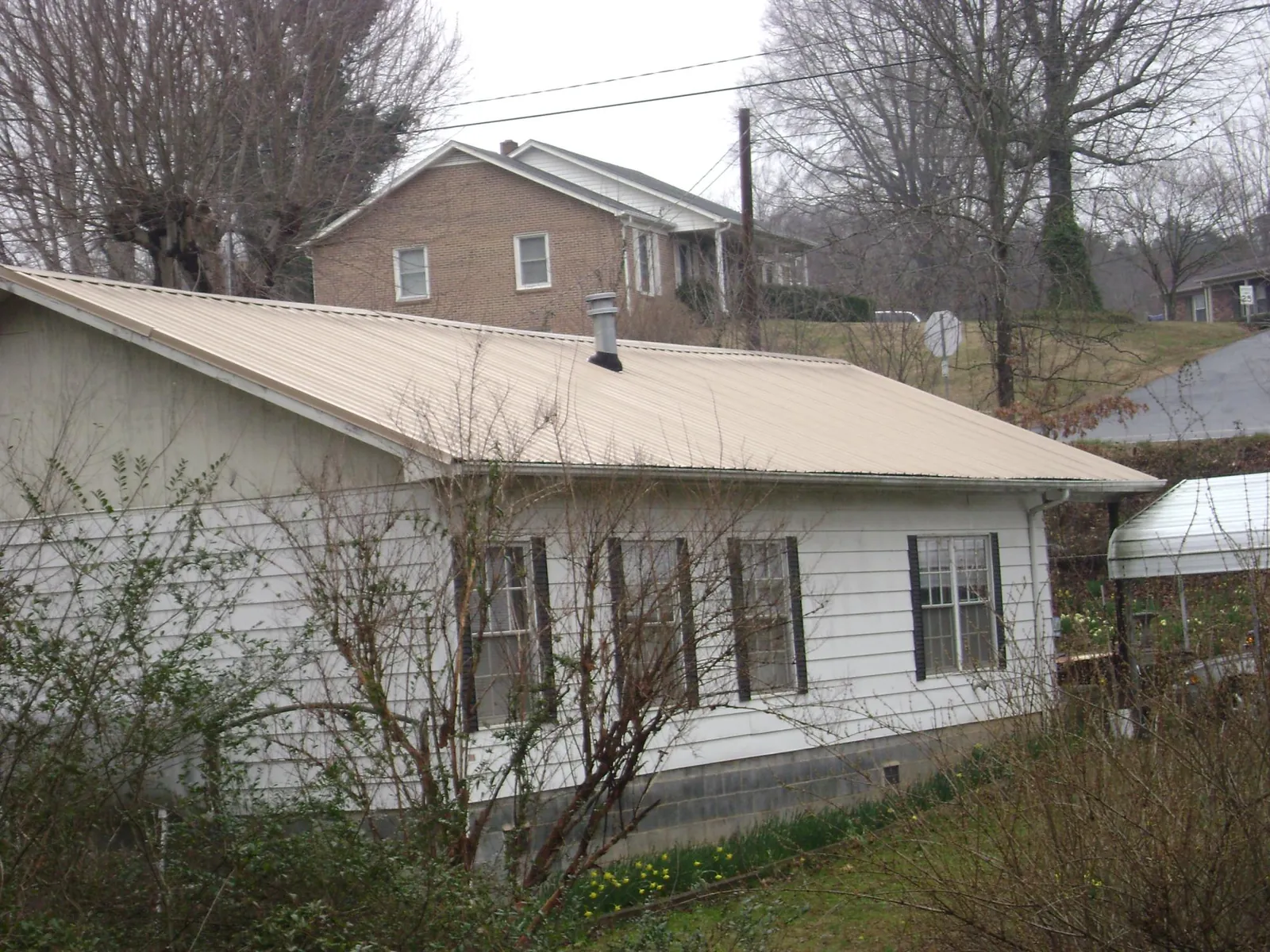 Tan metal roof on a white sided house set into a hillside — Commercial Roofing by Roofing Brothers in Thaxton