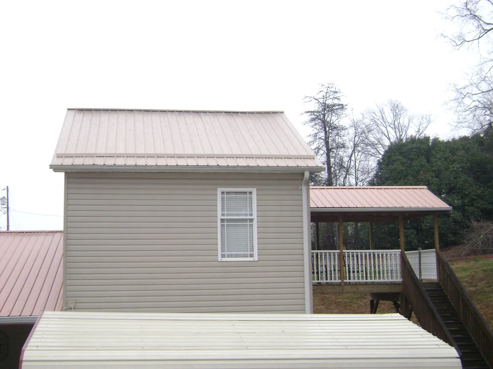 Tan metal roofs on a two story addition and attached porch, from a Roof Replacement job in Thaxton